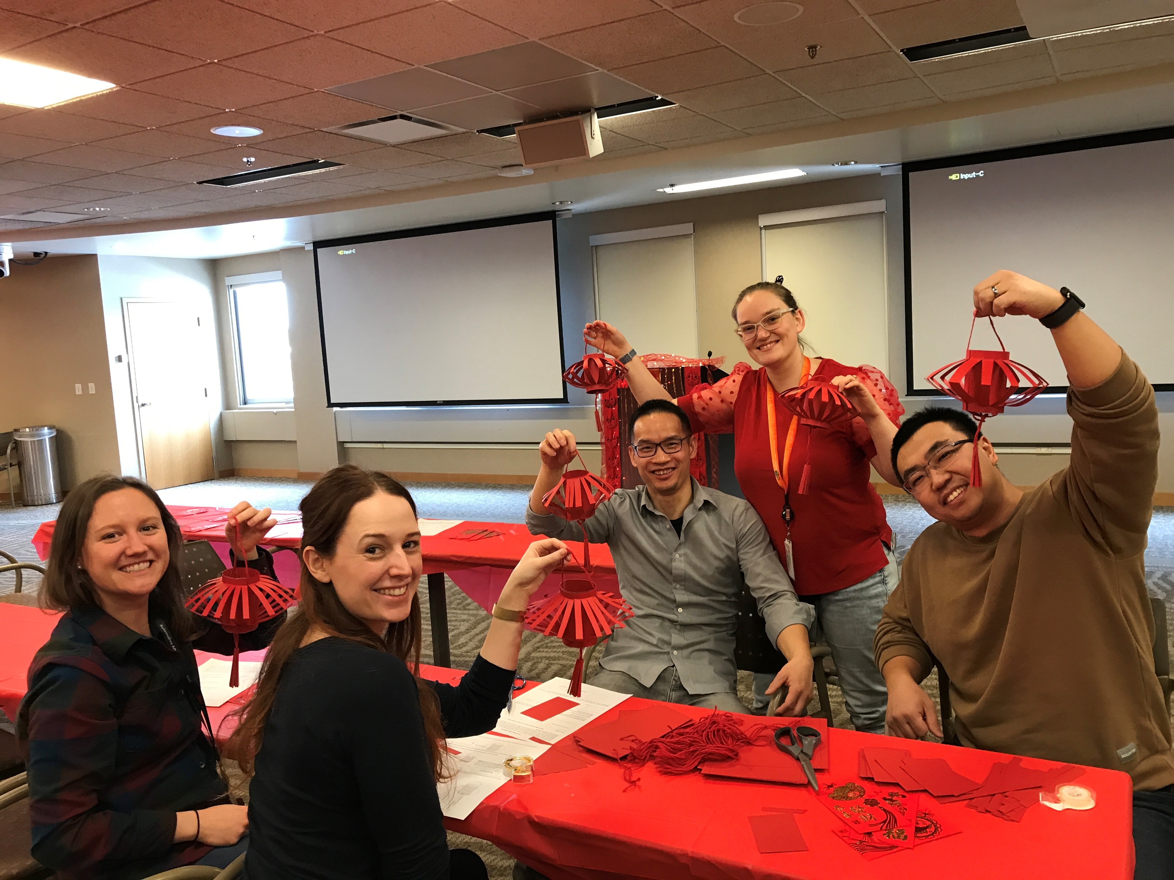 Five people holding up red lanterns in a conference room celebrating Diwali.