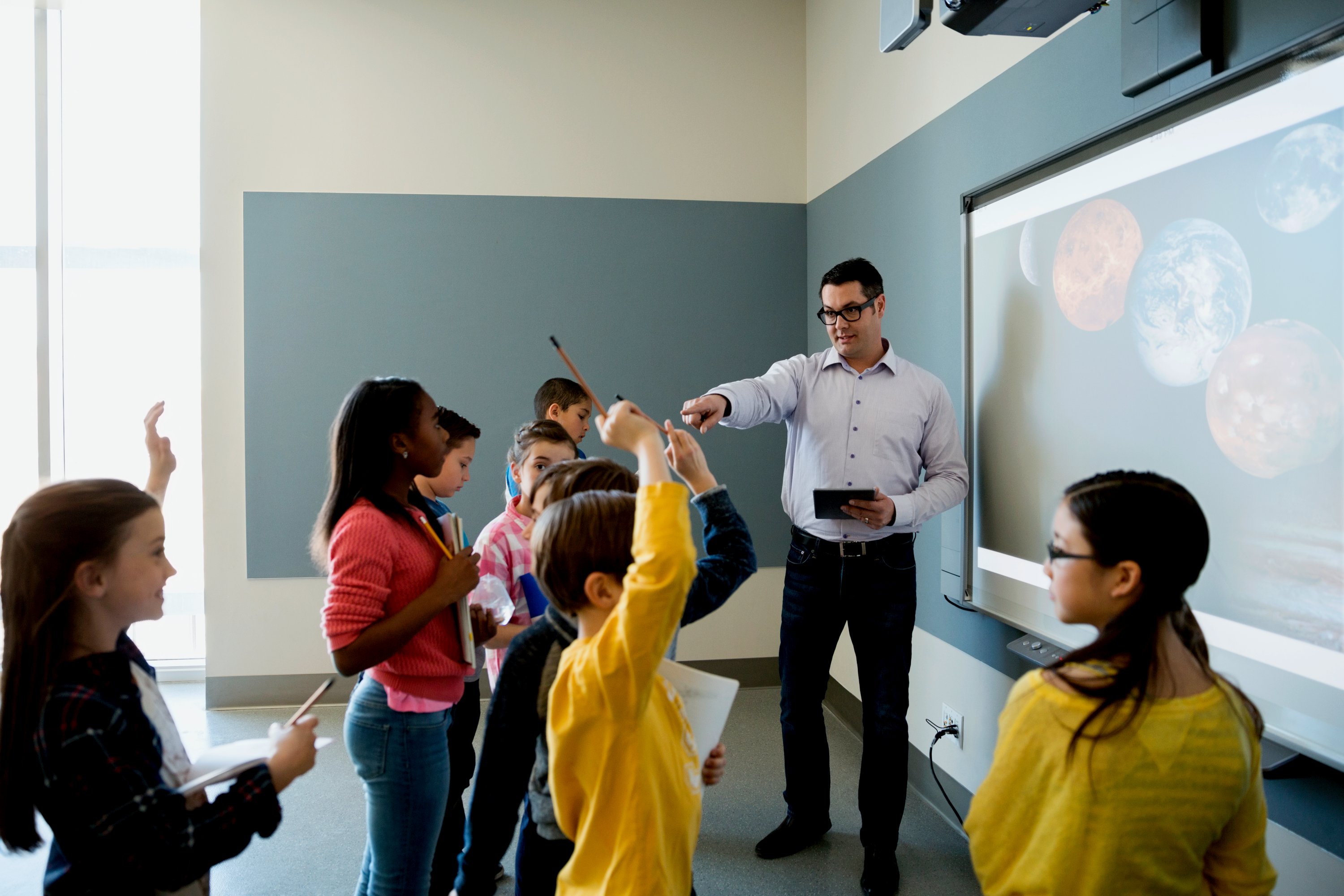 A man teaching a group of seven students around a projector.